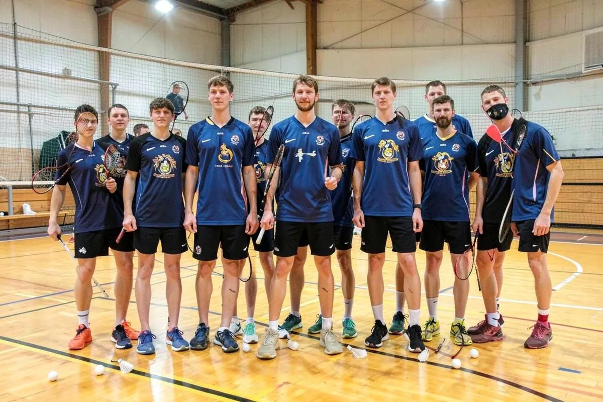 Badmintonmannschaft in einheitlichen Spielshirts mit Clubemblem auf dem Hallenfeld