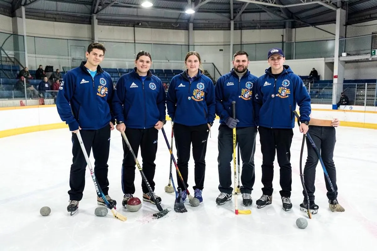 Curlingteam in einheitlichen Clubjacken mit Emblem auf dem Eis einer Curlinghalle