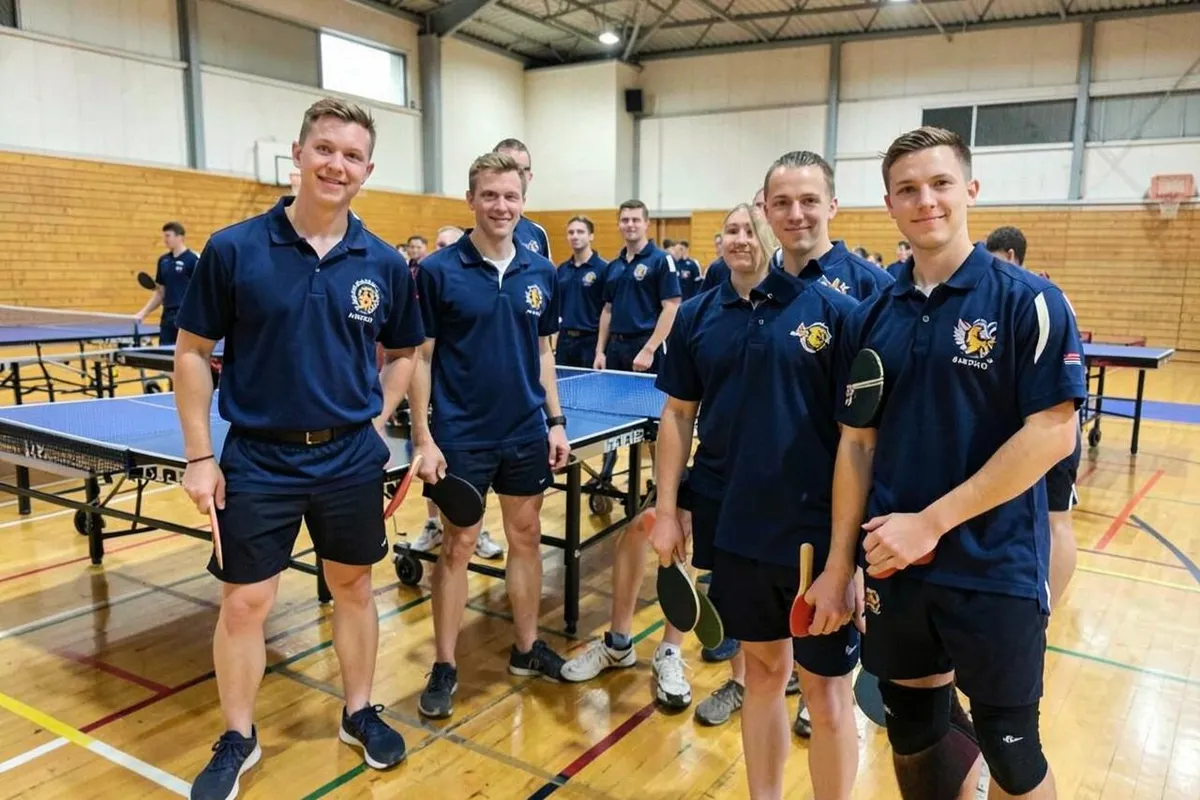 Tischtennismannschaft in einheitlichen Vereinspolos neben den Tischen in einer Sporthalle